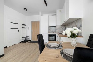 A modern kitchen with white cabinets, a wooden countertop, and a dining area with a table set for two. - Modern Apartment with a Balcony | A Place to Work (Chorzów)
