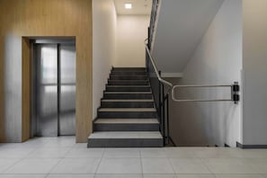 Ein modernes Interieur mit Treppe, Metallaufzug und Fliesenboden.