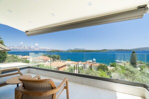 Ein Balkon mit Blick auf einen See und Berge, Holzmöbel und Geländer aus Glas.