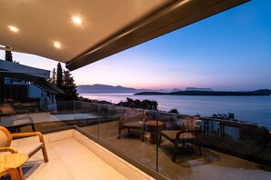 Ein Balkon mit Glasgeländer, der auf ein Gewässer und ferne Berge blickt.