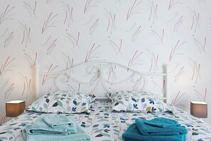 Una cama bien hecha con ropa de cama estampada, cabecera blanca y dos lámparas de noche.
