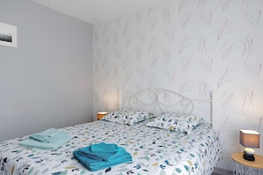 Una cama bien tendida con ropa de cama estampada, una lámpara de noche y una pared con diseño de hojas.