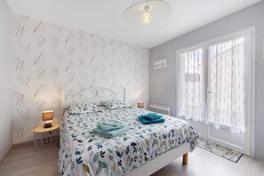 A bedroom with a bed, bedside lamps, a window with curtains, and a wall with a leaf pattern. - Guest Room 'Retour de Plage' – Sables D'Olonne (Les Sables-d'Olonne)