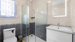 Kylpyhuone, jossa on lasiseinällä varustettu suihku, wc, pesuallas ja peili.