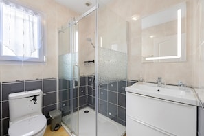 Un baño con ducha envuelta en vidrio, inodoro, lavamanos y espejo.