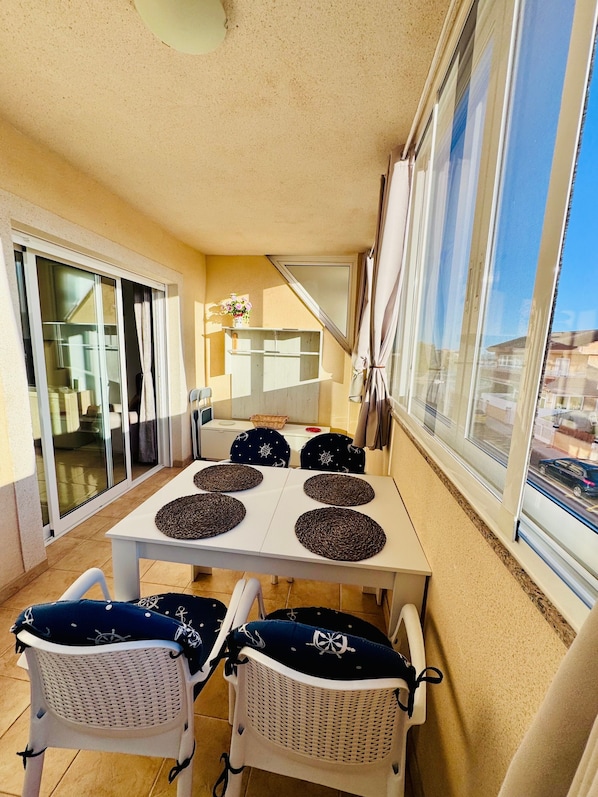 A balcony with a table and chairs, a sliding glass door, and a view of the street.