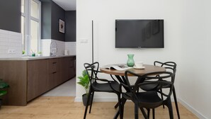 A modern kitchen with a dining area, a flat-screen TV mounted on the wall, and a potted plant. - A Functional Studio in the City Centre | Stary Browar (Poznań)