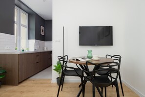 A modern kitchen with a dining area, a flat-screen TV mounted on the wall, and a potted plant. - A Functional Studio in the City Centre | Stary Browar (Poznań)