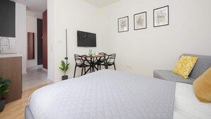 A modern hotel room with a large bed, a gray sofa, a dining table with chairs, and a flat-screen TV mounted on the wall. - A Functional Studio in the City Centre | Stary Browar (Poznań)