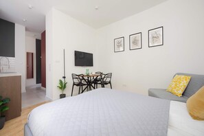 A modern hotel room with a large bed, a gray sofa, a dining table with chairs, and a flat-screen TV mounted on the wall. - A Functional Studio in the City Centre | Stary Browar (Poznań)