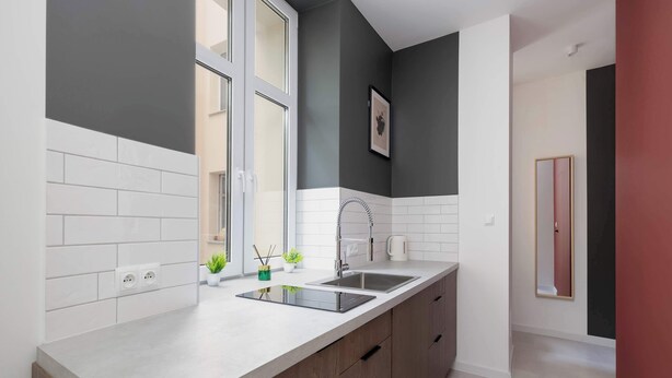A modern kitchen with a double sink, white tiled backsplash, and wooden cabinets. - A Functional Studio in the City Centre | Stary Browar (Poznań)