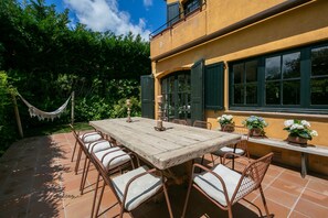 A patio with a wooden table and chairs, surrounded by potted plants and a hammock. - Villa 'Pastora' with Sea Views, Wi-Fi, and Air Conditioning (Llafranc)