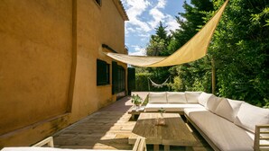 A sunlit outdoor seating area with a sofa, a wooden table, and a hammock.