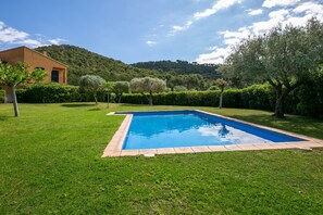 A rectangular swimming pool with a tiled edge, surrounded by well-maintained grass and hedges, with a mountain in the background. - Villa 'Pastora' with Sea Views, Wi-Fi, and Air Conditioning (Llafranc)
