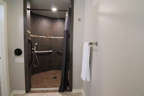 A shower area with a tiled floor, a handrail, and a towel rack.