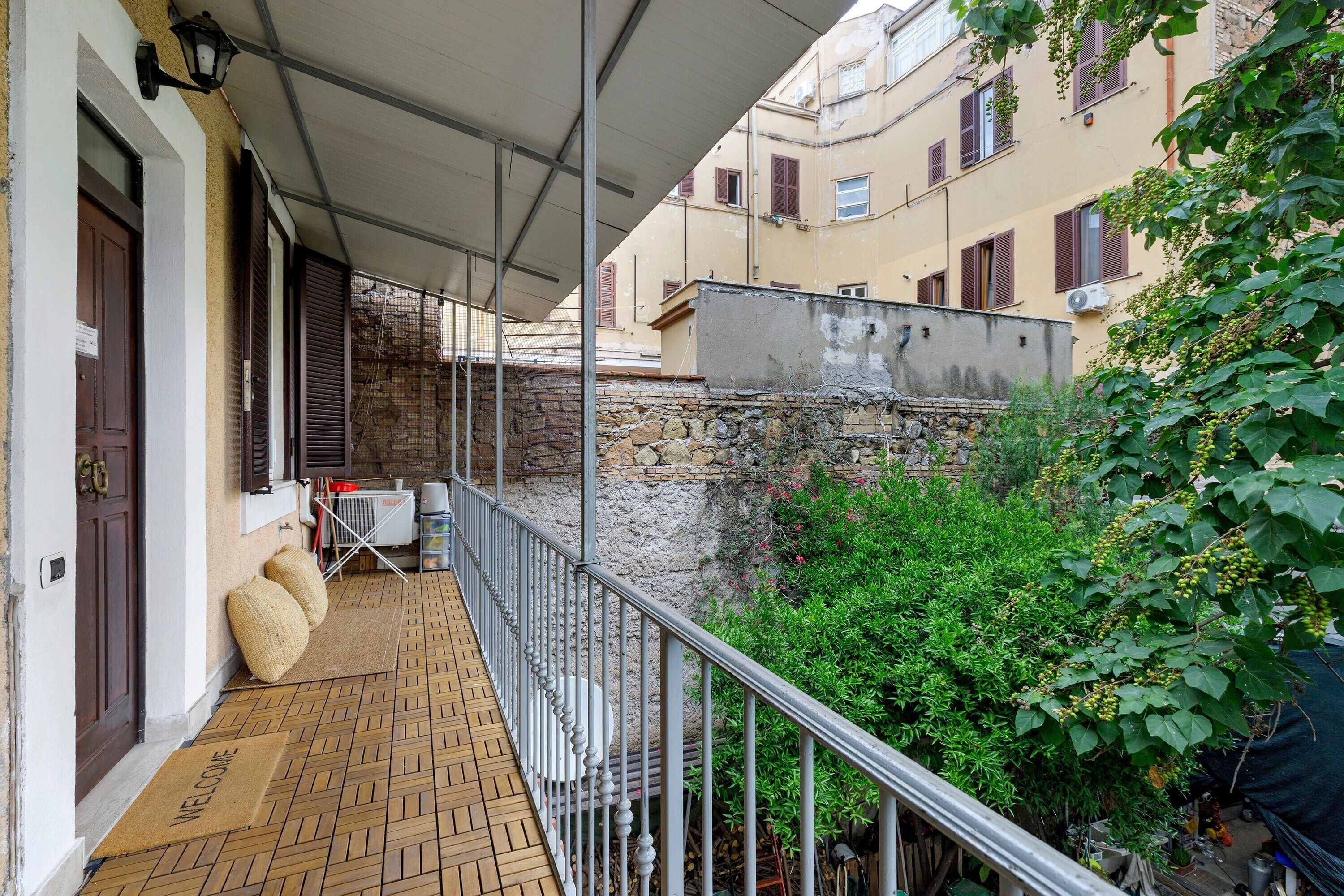 Un balcone con ringhiera in metallo, un tappetino d'ingresso e una porta con persiana marrone.