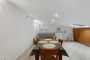 Uma área de refeições com uma mesa posta para quatro pessoas, um sofá, um radiador, um ventilador e uma porta.