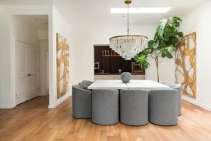 Uma sala de jantar moderna com uma mesa branca, pufes cinzentos, um candelabro e arte abstrata nas paredes.