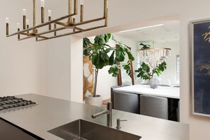 Une cuisine moderne dotée d’un évier en acier inoxydable, d’une cuisinière à gaz, d’un lustre et d’un coin repas avec une table et des chaises blanches.