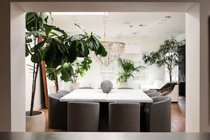 Un espace repas moderne avec une table blanche, des chaises grises et de grandes plantes en pot.