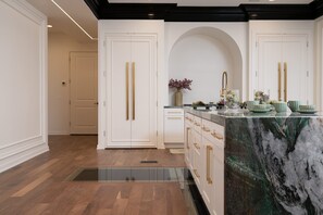 Uma cozinha moderna com armários brancos, uma ilha de mármore e piso de madeira.