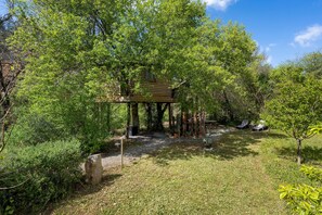A wooden treehouse elevated on stilts, surrounded by lush greenery, with a clear sky above.