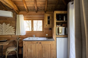 Interior de una cabaña de madera con una zona de cocina, que incluye un lavamanos, armarios y un refrigerador.