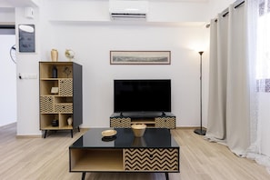 A modern living room with a flat-screen TV, a wooden cabinet with patterned shelves, a coffee table, and a floor lamp. - Apartment 'Ceramicist' with Shared Terrace, Wi-Fi and Air Conditioning (Heraklion)