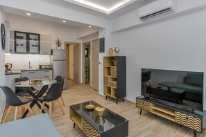 A modern living room with a flat-screen TV, a glass dining table with chairs, a black coffee table, and a kitchen area with cabinets and a refrigerator. - Apartment 'Ceramicist' with Shared Terrace, Wi-Fi and Air Conditioning (Heraklion)