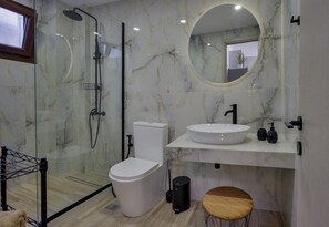 Un baño moderno con ducha envuelta en vidrio, inodoro, lavamanos con espejo y un taburete pequeño.