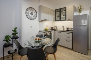 Una cocina moderna con una mesa de comedor de vidrio, sillas negras, un refrigerador de acero inoxidable y un reloj en la pared.