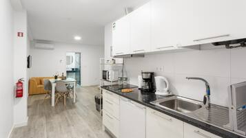Una cocina moderna con armarios blancos, un lavamanos de acero inoxidable y una cafetera.