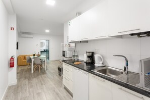 Una cocina moderna con armarios blancos, un lavamanos de acero inoxidable y una cafetera.