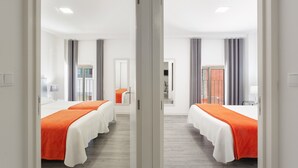 Quarto de hotel com duas camas, um espelho, uma janela com cortinas e uma porta.