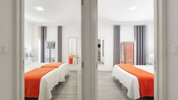 Habitación de hotel con dos camas, un espejo, una ventana con cortinas y una puerta.