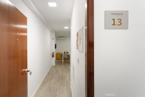 Um corredor com uma porta de madeira, uma placa com o número 13 e uma área de jantar ao fundo.