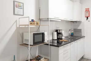 Una cocina moderna con gabinetes blancos, microondas, cafetera y un lavamanos.