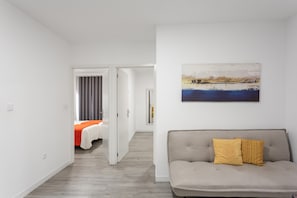 Una habitación de hotel moderna con sofá, cama con colcha naranja y un cuadro en la pared.