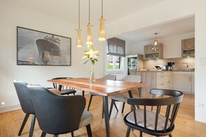 Eine moderne Küche mit Holzausstattung, ein Essbereich mit Holztisch und Stühlen sowie ein großes Schiffsbild an der Wand.