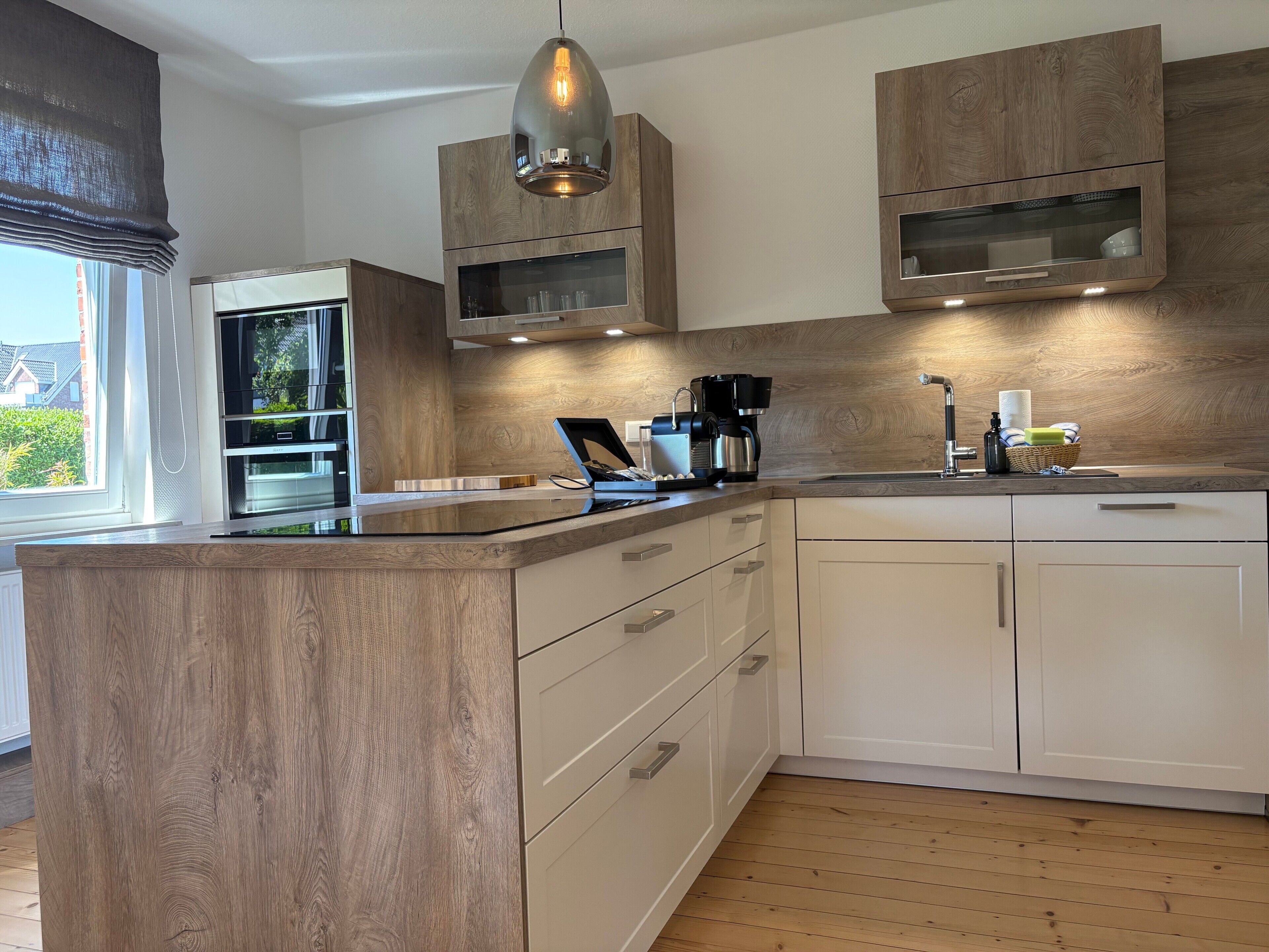 A modern kitchen with wooden cabinetry, a built-in oven, a coffee maker, and a window with a view of greenery.