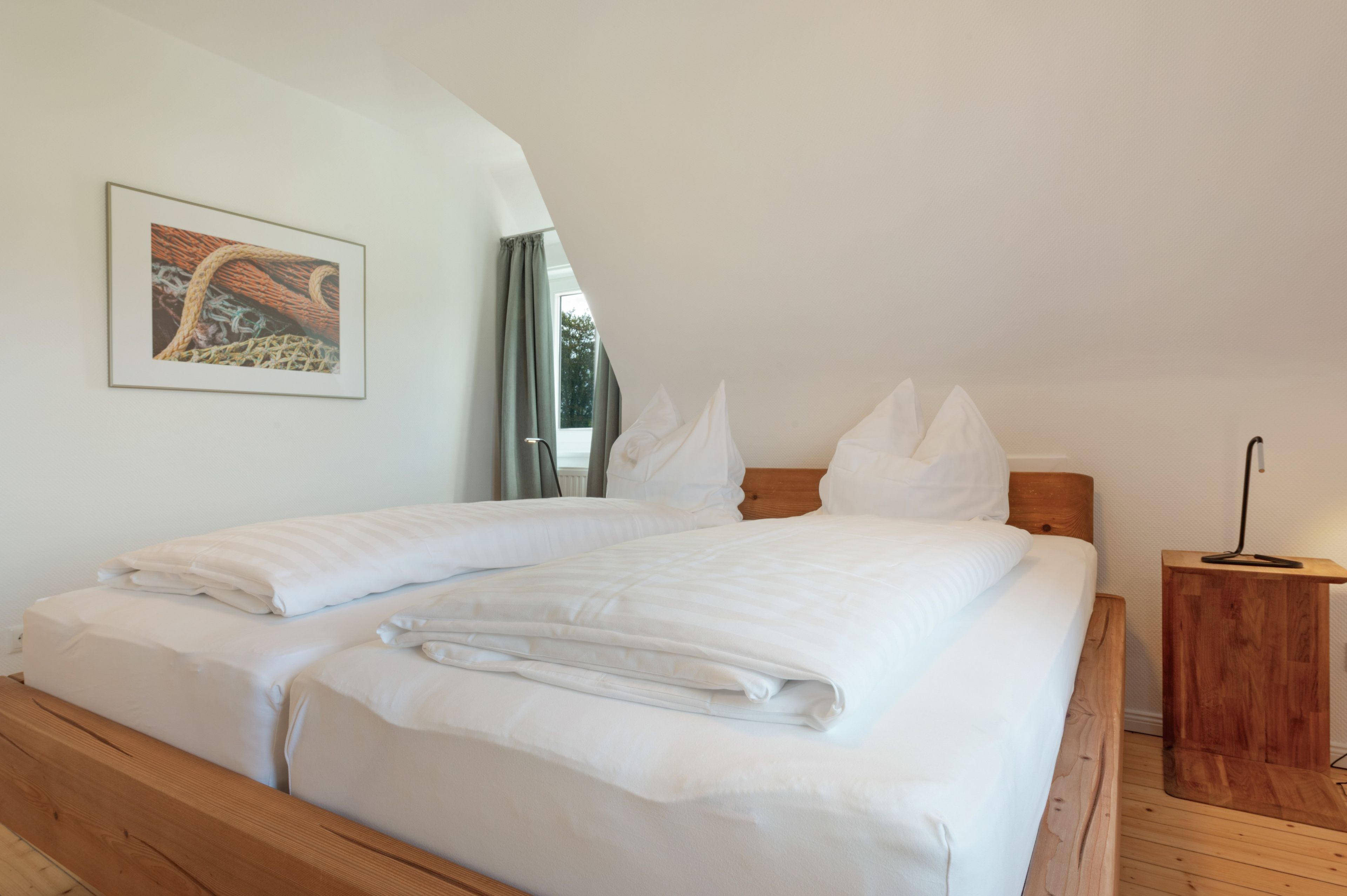A neatly made double bed with white linens, a wooden headboard, and a small bedside table with a lamp.