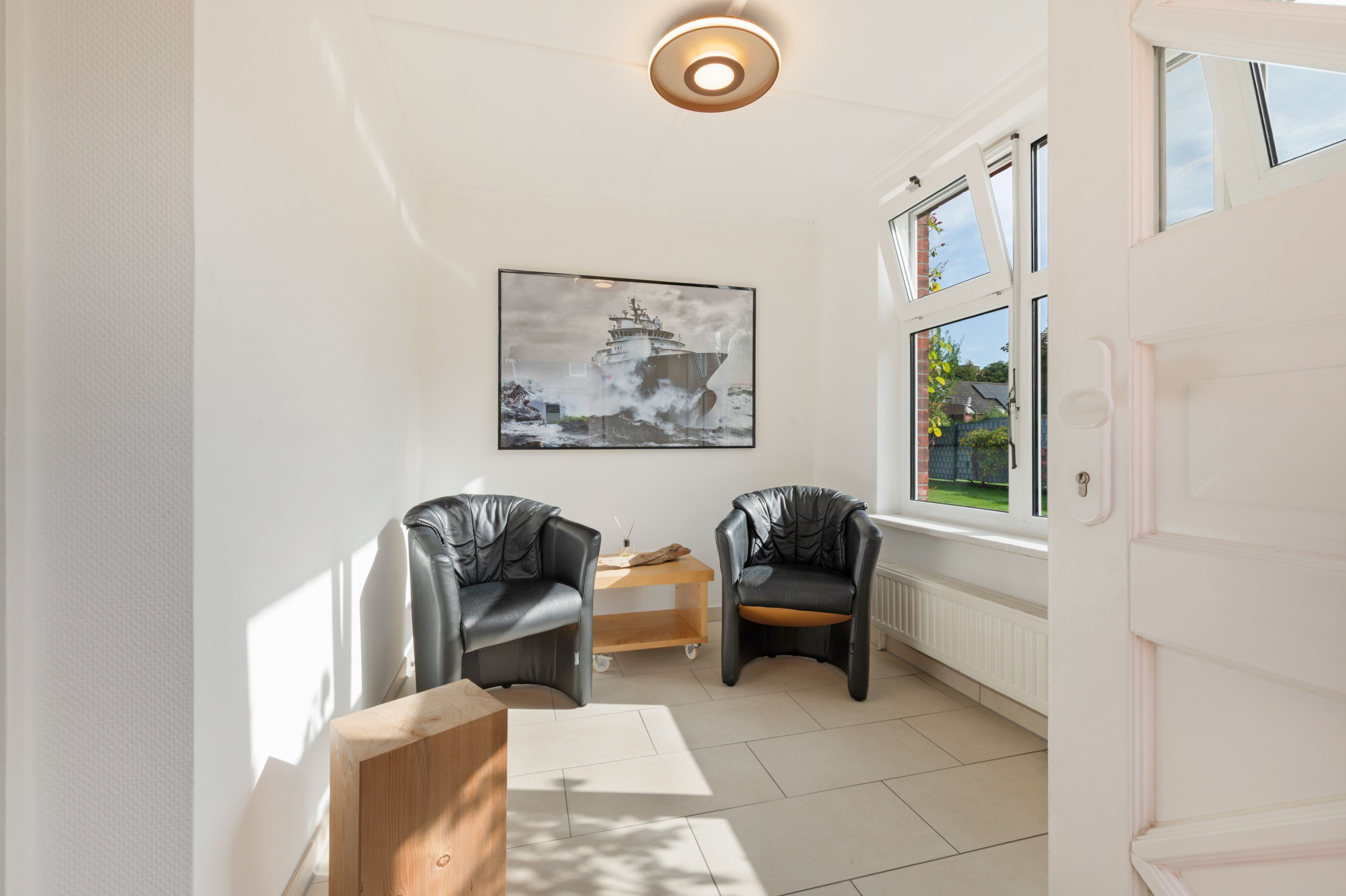 A modern room with two leather chairs, a wooden table, a framed picture on the wall, and a window with a view of greenery.
