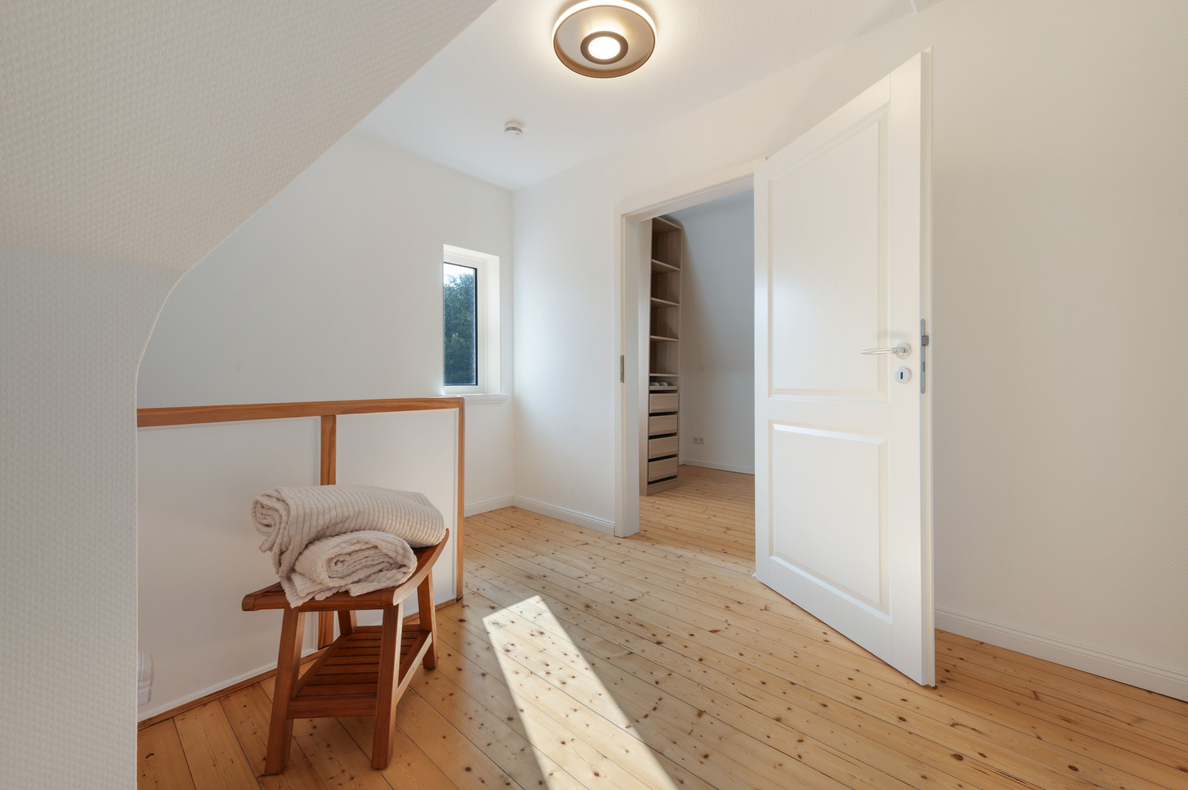 A room with a wooden chair, a small window, and a closet with wooden doors.