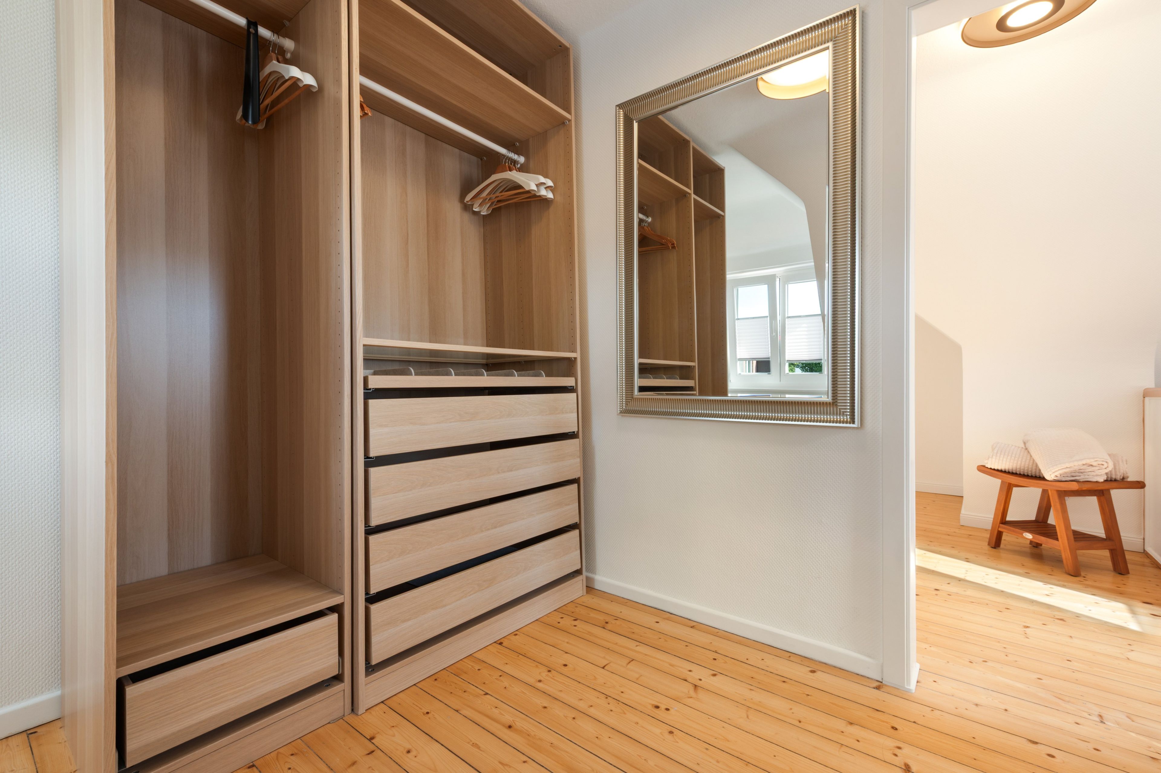 A walk-in closet with wooden drawers and shelves, a mirror, and a wooden stool.