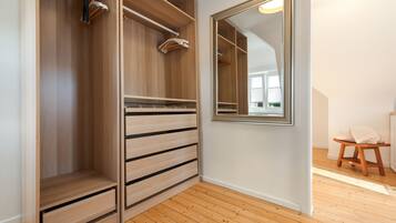 A walk-in closet with wooden drawers and shelves, a mirror, and a wooden stool.