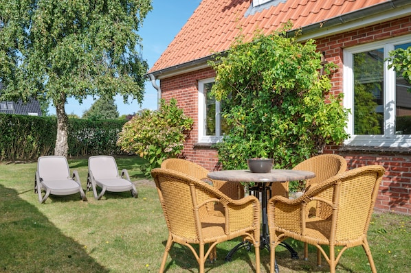 Une terrasse dotée de meubles en osier et d’une table, entourée d’une maison en briques et de verdure.