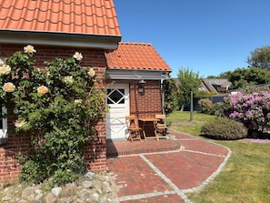 Ein Backsteinhaus mit Ziegeldach, einer weißen Tür und einer kleinen Terrasse mit Tisch und Stühlen.