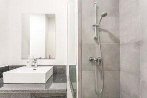 Een badkamer met een wit wastafel, een spiegel en een douche met een handdouche.