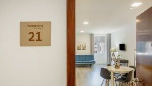 A hotel room with a wooden door, a sign with the number 21, a dining area with a table and chairs, a blue sofa, and a TV on the wall. - Tanoeiros Studio - Spacious and Comfortable Accommodation (Funchal)