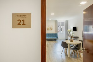 A hotel room with a wooden door, a sign with the number 21, a dining area with a table and chairs, a blue sofa, and a TV on the wall. - Tanoeiros Studio - Spacious and Comfortable Accommodation (Funchal)